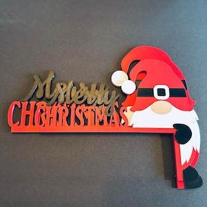 Two layered Merry Christmas gnome door corner cutout pieces stacked on a dark grey surface, showing depth and details.