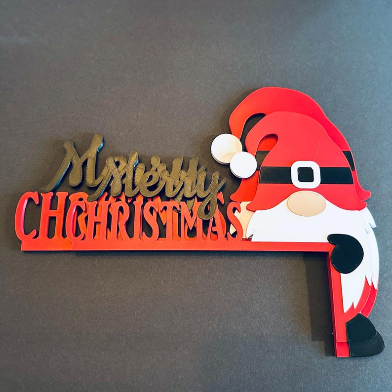 Two layered Merry Christmas gnome door corner cutout pieces stacked on a dark grey surface, showing depth and details.