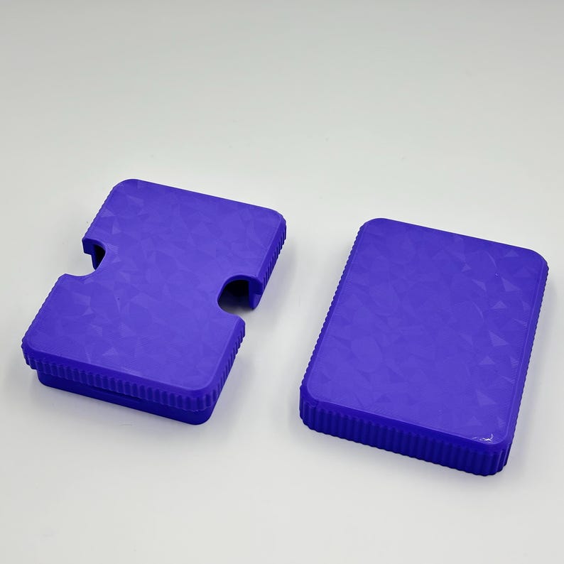 May include: Two blue plastic cases with textured surfaces. One case has a unique cutout shape, while the other is rectangular. Both cases have a ridged border. The cases are likely for storing or protecting items.