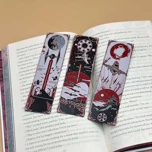 May include: Three Star Wars-themed bookmarks are displayed on an open book. Each bookmark features a different design with spaceships, planets, and red and white color schemes. The bookmarks are rectangular and made of a glossy material.