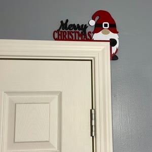A slightly angled shot of the top right corner of a white door featuring the festive gnome decoration on a grey wall.