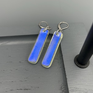 May include: A pair of iridescent blue glass earrings with silver hooks. The earrings are rectangular in shape and have a subtle shimmer.