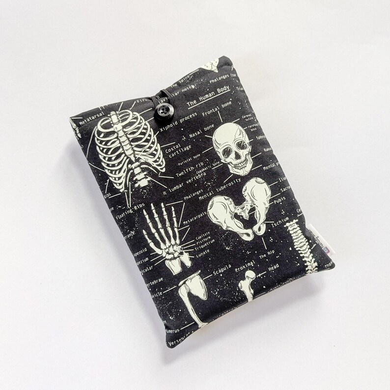 May include: Black and white padded case featuring a skeletal diagram of the human body. The case has a button closure and includes labeled illustrations of bones and anatomical structures. The text "The Human Body" is visible.