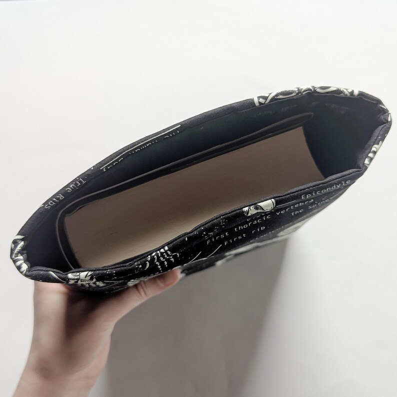 May include: Black and white fabric sleeve with a skeletal anatomy print. The sleeve is open, revealing a light brown interior. The text on the fabric includes anatomical terms like "true ribs" and "first rib".