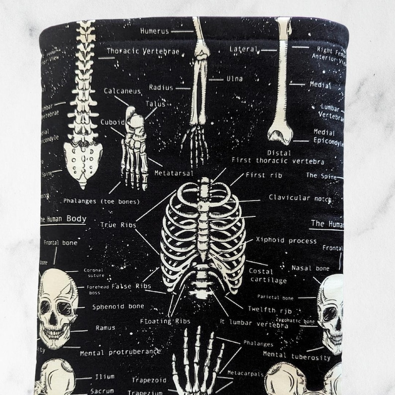 May include: Black and white anatomical print featuring detailed illustrations of the human skeletal system, including the skull, spine, ribs, and various bones. The text labels the different parts of the skeleton. The background is black.
