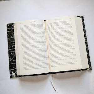 May include: An open book with black covers and a black bookmark. The pages are filled with printed text. The left cover has a black and white design with anatomical terms. The book is open to pages 148 and 149.