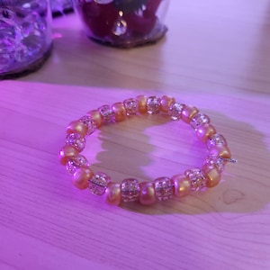 May include: A gold and clear beaded bracelet with a sparkly finish.