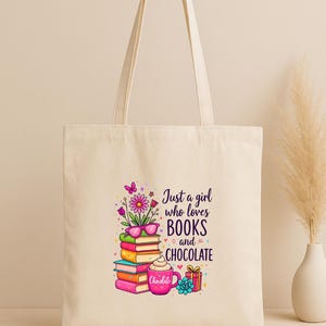 May include: Cream-colored tote bag with a colorful graphic. The graphic features a stack of books, flowers, butterflies, and a cup of chocolate. Text reads: "Just a girl who loves BOOKS and CHOCOLATE."