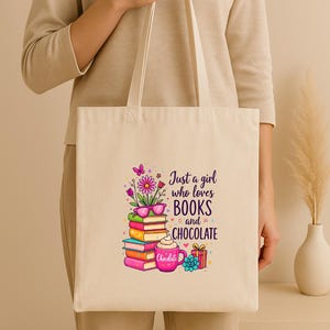 May include: Cream-colored tote bag with the text "Just a girl who loves BOOKS and CHOCOLATE." The graphic includes a stack of books, a coffee mug, and a gift box. The bag is held by a person.