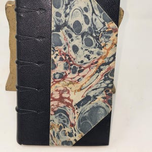 May include: A black leather-bound book with a marbled paper cover. The marbling is in shades of blue, red, and white.