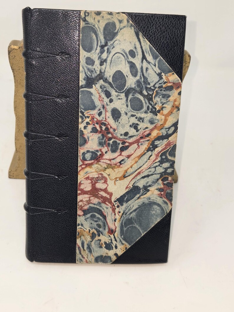 May include: A black leather-bound book with a marbled paper cover. The marbling is in shades of blue, red, and white.