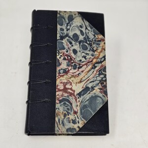 May include: A small black leather-bound journal with a marbled paper cover. The journal has a decorative spine with stitching.