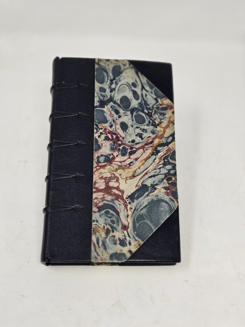 May include: A small black leather-bound journal with a marbled paper cover. The journal has a decorative spine with stitching.