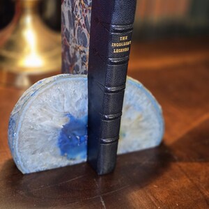 May include: A book titled "The Ingoldsby Legends" is propped up by a blue and white agate bookend. The bookend is made of natural stone and has a unique, organic shape.