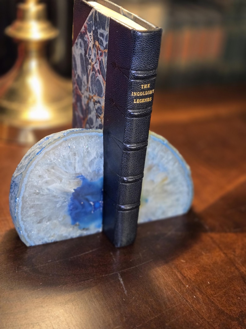 May include: A book titled "The Ingoldsby Legends" is propped up by a blue and white agate bookend. The bookend is made of natural stone and has a unique, organic shape.