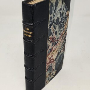 May include: A black leather-bound book with gold lettering on the spine that reads "The Ingoldsby Legends". The book has a marbled paper cover.