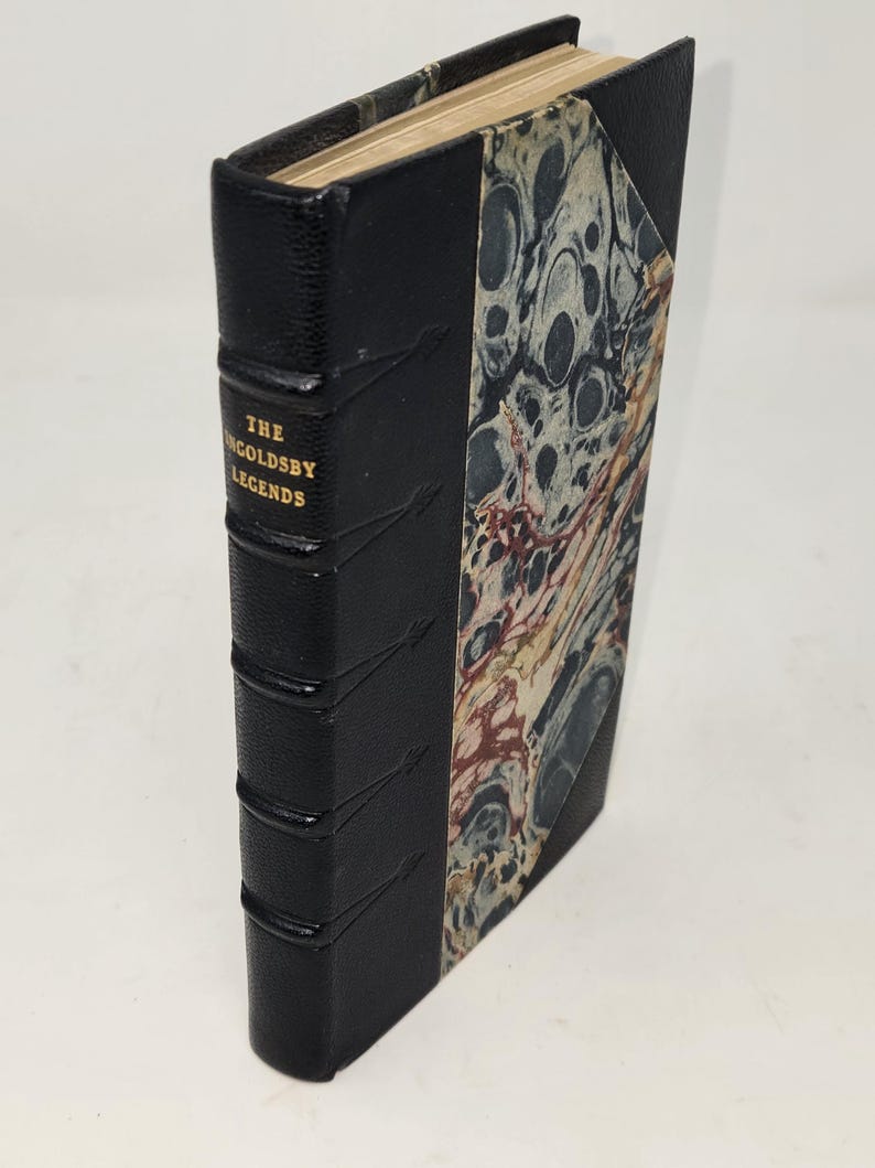 May include: A black leather-bound book with gold lettering on the spine that reads "The Ingoldsby Legends". The book has a marbled paper cover.