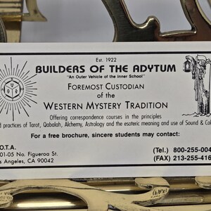 Puede incluir: Una tarjeta de presentaci&oacute;n de Builders of the Adytum, establecida en 1922. La tarjeta presenta informaci&oacute;n sobre la Tradici&oacute;n del Misterio Occidental, incluyendo Tarot, C&aacute;bala y Alquimia. La tarjeta est&aacute; sobre un elemento decorativo dorado.