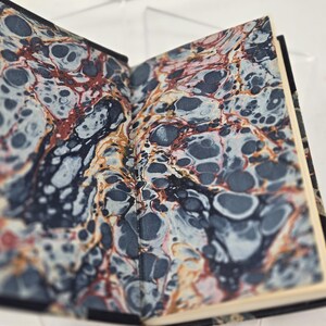 May include: A book with a marbled cover in shades of blue, red, and white. The marbling pattern is reminiscent of swirling water.