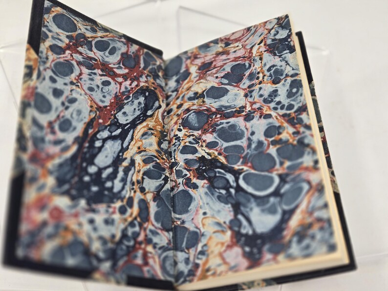 May include: A book with a marbled cover in shades of blue, red, and white. The marbling pattern is reminiscent of swirling water.