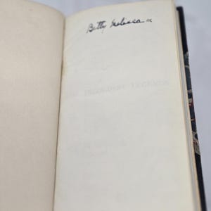May include: An open book with a white page and a black inscription that reads "Betty Roberts". The book has a dark blue cover with a patterned design.