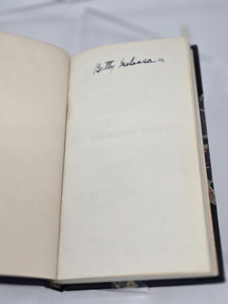 May include: An open book with a white page and a black inscription that reads "Betty Roberts". The book has a dark blue cover with a patterned design.