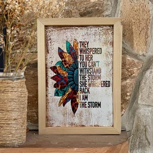 May include: A framed print with a colorful sunflower design and the text "They whispered to her you can't withstand the storm she whispered back I am the storm".