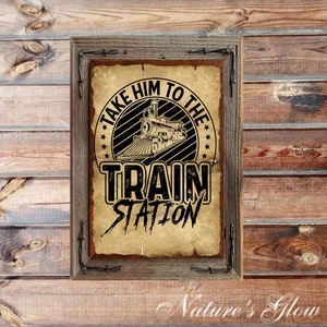 May include: A framed rustic sign with the text "TAKE HIM TO THE TRAIN STATION" and a vintage train illustration. The sign is set against a wooden background, with a weathered paper appearance and a wooden frame.