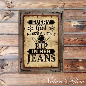 May include: A rustic wooden framed sign with the text "EVERY Girl NEEDS A LITTLE RIP IN HER JEANS". The sign features a cowboy hat graphic and sheriff star accents, set against a parchment-style background. The frame is made of weathered wood.
