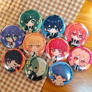 May include: A collection of ten round, colorful anime-style character buttons. Each button features a different character with unique hair and eye colors, dressed in various outfits. The buttons are arranged on a brown and white checkered surface.