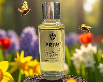 May include: A clear glass perfume bottle with a silver cap, containing a pale yellow liquid. The label reads PRIM' Galimard Parfumeur en 1747 GRASSE FRANCE. A butterfly and a bee are positioned on either side of the bottle.