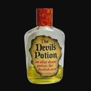 May include: A clear glass bottle of "The Devil's Potion" aftershave. The label is a tan colour with black and red text. The bottle has a red and yellow patterned cap and contains a yellow liquid.