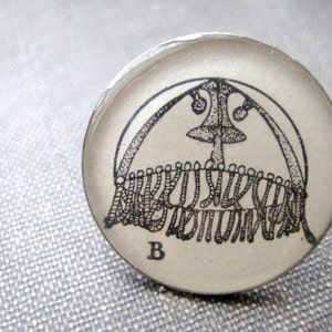 May include: A white, round, glass cabochon with a black and white illustration of a jellyfish with the letter "B" printed on the bottom.