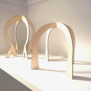 Peut inclure: Trois structures en forme d'arche en bois, avec une finition marron clair, sont disposées sur une surface blanche. Les arches ont un design minimaliste, avec une base plate et un sommet incurvé. Les structures sont espacées uniformément.