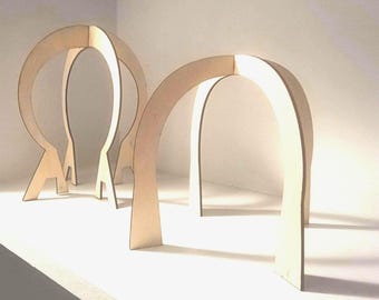 Puede incluir: Tres estructuras de madera en forma de arco con un acabado marrón claro están dispuestas sobre una superficie blanca. Los arcos tienen un diseño minimalista, con una base plana y una parte superior curvada. Las estructuras están espaciadas uniformemente.