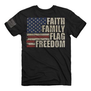 May include: Black t-shirt with a distressed American flag design and the words "Faith Family Flag Freedom" printed on it.