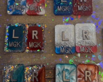 May include: Nine small square tiles with different colored backgrounds and glitter. Each tile has a silver letter 'L' or 'R' and the text 'MGK' on it. The tiles are for marking left and right.