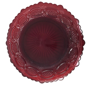 May include: A ruby red glass plate with a scalloped edge and intricate embossed detailing. The plate features a central sunburst pattern and a decorative border with oval and diamond-shaped designs. This vintage-style plate is suitable for serving or display.