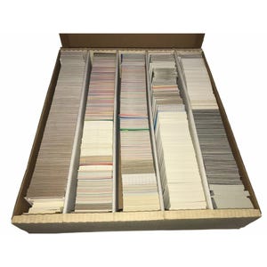 Könnte beinhalten: Ein rechteckiger Karton gefüllt mit Stapeln von Sammelkarten, getrennt durch Kartontrenner. Die Karten weisen verschiedene Farben und Designs auf, was auf eine vielfältige Sammlung hindeutet.