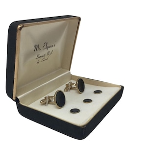 May include: A black velvet box with a gold trim, containing a set of cufflinks and studs. The box is labeled "Mc. Elgunn's Summit N.J. by Swank."
