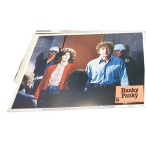 May include: A vintage movie poster for the film "Hanky Panky" featuring Gene Wilder and a woman in a red sweater. The poster has a retro aesthetic with a warm color palette and the title in a bold, orange font.