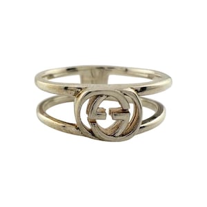 May include: Silver-toned ring featuring a double-band design. The ring showcases the iconic interlocking GG logo in the center, a signature element of the brand. The ring is a classic piece of jewelry.