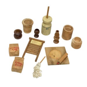 Könnte beinhalten: Eine Sammlung von Miniatur-Küchenartikeln aus Holz, darunter ein Butterfass, ein Waschbrett und ein Schneidebrett. Zwei kleine Papiertüten sind mit "Michael Reid" und "Kinnaird Reid" beschriftet. Die Artikel sind in verschiedenen Braun- und Beigetönen gehalten.