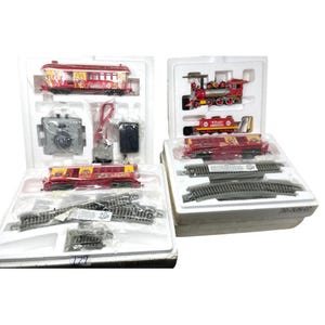 May include: Two boxed toy train sets. One set includes a red and yellow passenger carriage, a control box, and track pieces. The other set features a red locomotive, a passenger carriage, and track. Both sets are in their original packaging.