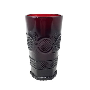 May include: A tall, ruby-red glass with a textured, geometric pattern. The glass features a diamond and circle design around the middle and a textured base. The rim of the glass is a deep red color.
