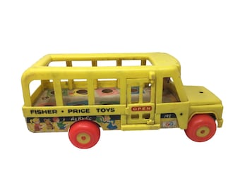 Puede incluir: Autobús escolar de juguete de plástico amarillo con interior de madera y puertas abiertas. El autobús tiene ruedas rojas y dice "Fisher-Price Toys" en el lateral. El autobús tiene un letrero que dice "Abierto" y un número "192" en el lateral.