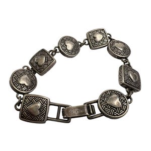 K&ouml;nnte beinhalten: Silberfarbenes Armband mit abwechselnd quadratischen und runden Gliedern, die jeweils mit einem Herzmotiv verziert sind. Die Glieder haben ein strukturiertes Muster. Der Verschluss ist mit dem Markennamen "Brighton" versehen.