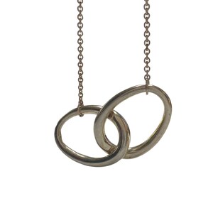 May include: Silver-toned necklace featuring two interlocking oval pendants suspended from delicate chains. The pendants are smooth and polished, creating a minimalist and elegant design. The necklace is set against a plain white background.