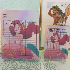 May include: Two rectangular scorecards featuring a cartoon mermaid with long red hair and a floral dress. Each card includes a grid for Game 1, Game 2, and Game 3 with columns for Play/Draw and Win/Loss, plus fields for Round, Player 1, and Player 2.