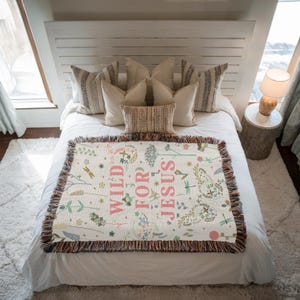 May include: A white woven throw blanket with a floral pattern and the text "WILD FOR JESUS" in pink lettering.
